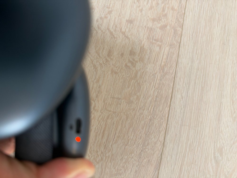 手に持ったAirPods Maxの右側の下の面。USB-Cの差込口の下で、小さなランプがオレンジ色に光っている